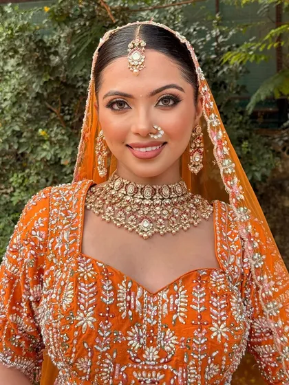 A full-face portrait showing the complete look. The soft makeup beautifully complements the vibrant orange of her outfit.