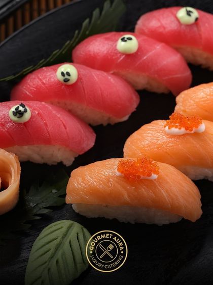Freshly sliced tuna and salmon nigiri, artfully arranged on a black plate with a wasabi leaf and a rose made of pickled ginger. We believe every detail matters when it comes to luxury catering.