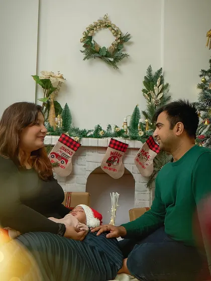 A family gazes lovingly at their newborn, nestled by a cozy fireplace setup during a Christmas mini session. It’s a heartwarming scene of a family's first holiday together.