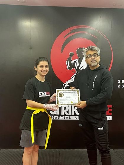 A female student proudly holds her certificate after successfully passing her kickboxing belt test.