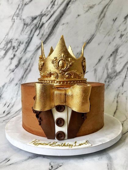 A cake fit for a king! This design features a tuxedo-style finish with a fondant bow tie and is topped with an intricate, hand-molded golden crown. It's the perfect centerpiece for celebrating the main man in your life.