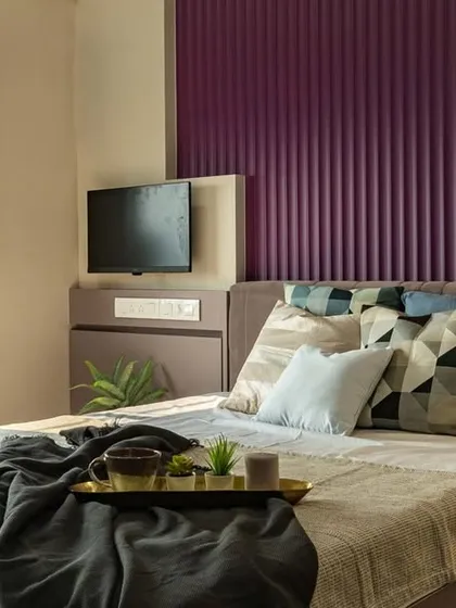 A cozy reading nook by the window in a master bedroom. The design features a vibrant purple fluted panel behind the bed, adding a pop of color and texture to the neutral space.