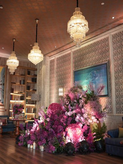 Inside the Mehendi venue, a massive floral installation in shades of pink becomes the centerpiece of the room. The design complements the venue's luxurious interiors, with classic chandeliers and patterned walls, creating a look of opulent romance.