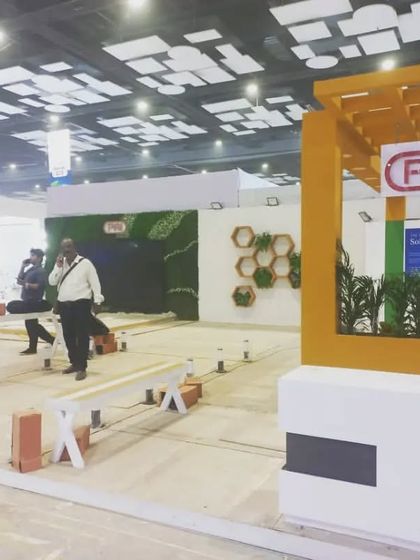 The PAI booth setup is in progress, featuring a warm yellow structure and natural plant elements.