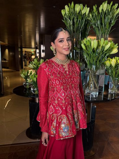 A full view of this chic Mehendi look. The makeup is subtle and clean, allowing the vibrant red outfit and intricate hairstyle to be the main focus.