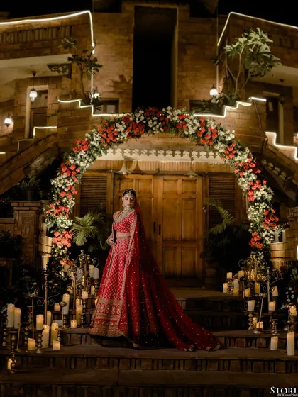 The bride standing at the entrance of the palace, her magnificent red lehenga spread out on the stairs, creating a truly royal image.
