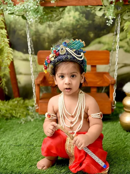 A classic portrait of a baby boy as Lord Krishna. His direct gaze and traditional accessories, including the pearl necklaces and flute, make for a powerful and adorable photograph.