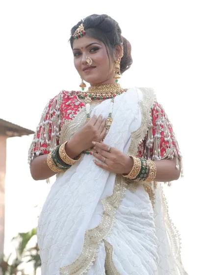 A confident bride in a white and red ensemble. Her makeup is kept fresh and radiant, with a focus on glowing skin and defined eyes, complementing her beautiful smile.