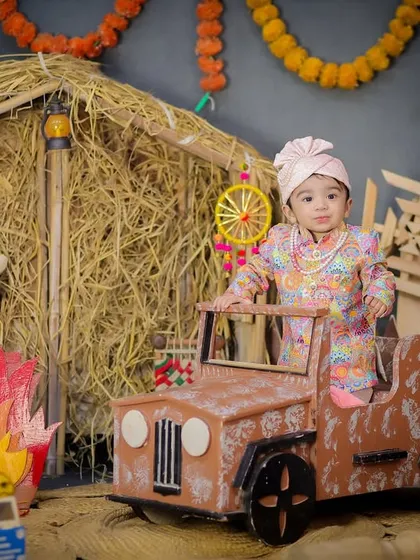 This little sardar is celebrating his first Lohri in style, sitting in a mini jeep with a bonfire prop and festive decorations all around.