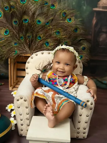 A happy baby Krishna holding his flute, ready to charm everyone. The peacock feather backdrop adds a touch of divine beauty.
