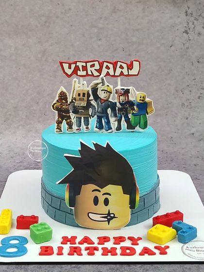 A cool Roblox-themed cake for an 8th birthday. This blue cake features a large Roblox face, character toppers, and edible building blocks.