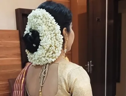 A close-up of the bride's hair and the back of her blouse. The saree's pallu is neatly pinned to stay in place, showcasing the full beauty of her wedding look.
