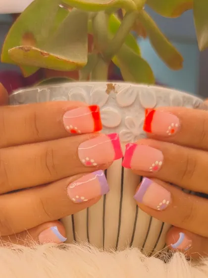 A close-up of a creative French manicure with multi-colored tips and delicate white dot accents, perfect for a fun, summery vibe.