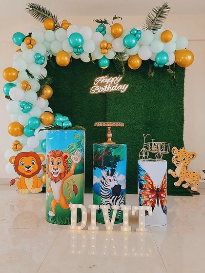 A fresh take on the jungle theme with custom-printed pedestals featuring animal prints. This setup combines a green grass backdrop, a teal and gold balloon garland, and cute lion cutouts for a bright and cheerful safari birthday party.