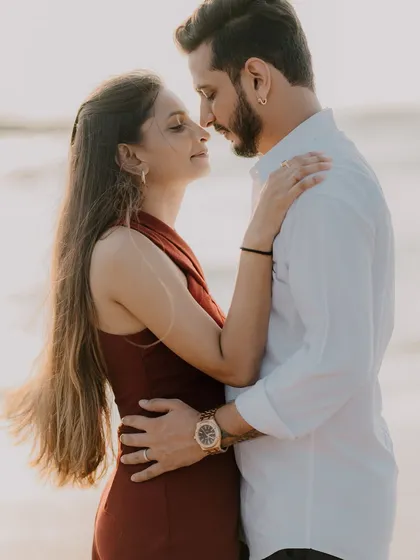 An intimate close-up of the couple on the beach. The warm sunset light and their gentle embrace create a very romantic and peaceful mood.