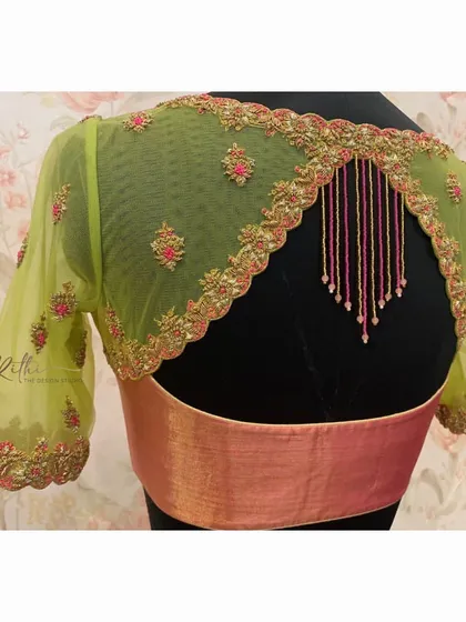 A unique back design on a lime green net blouse. The scalloped cutwork is highlighted with pink and gold embroidery, and beaded tassels add a playful touch.