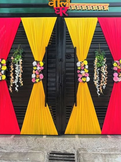 A simple and traditional decoration for the main gate of a wedding house. The gate is adorned with red and yellow drapes and floral bouquets to welcome guests.