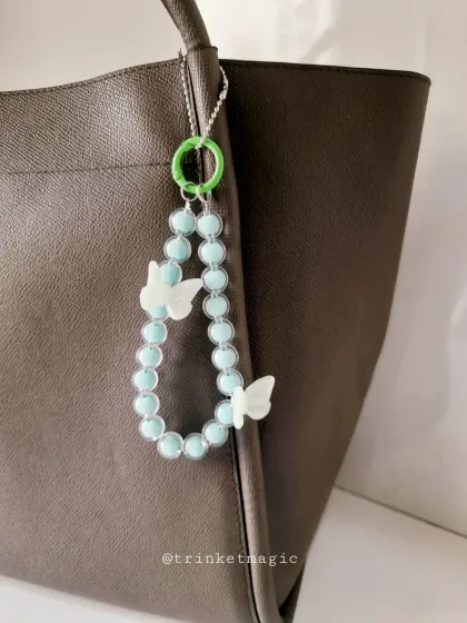 This minty blue-green beaded bag charm with white butterfly accents is fresh and fun. The bright green clasp adds an extra pop of color.