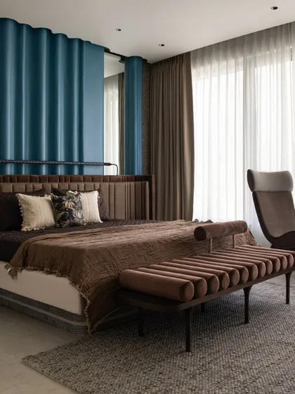 A full view of the master bedroom, highlighting the balance between the bold blue ripple wall and the warm, earthy tones of the custom furniture. The large windows are dressed in dual-layered drapery to gently filter natural light, creating a serene and relaxing atmosphere.