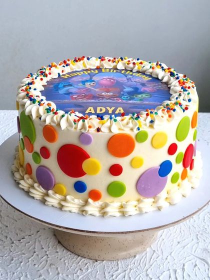 An "Inside Out" themed cake with a simple buttercream finish. The design uses fondant polka dots and an edible image on top.