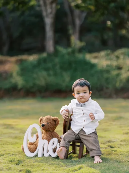 A classic portrait of the birthday boy sitting on a small chair with his teddy bear, looking very dapper for his big day.