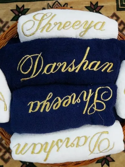 A beautiful trousseau hamper for a bride and groom. This set features a mix of navy and white towels, all personalized with their names and initials in elegant gold script, presented in a rustic wicker basket.