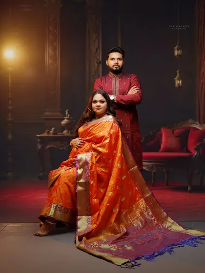 A regal portrait of the couple in our studio. The dramatic lighting and classic seating arrangement create a formal and timeless image, highlighting the beautiful drape of the saree.