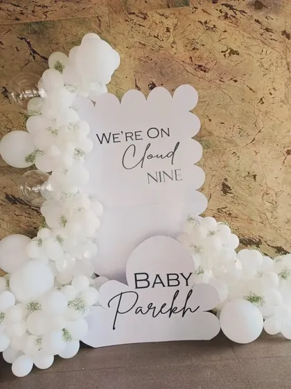 A chic and minimalist "We're on Cloud Nine" baby announcement decoration. The all-white design with cloud-shaped balloons and elegant script creates a clean and sophisticated look.