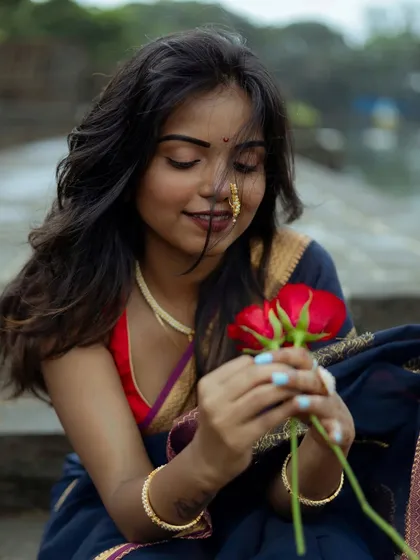 A soft, romantic portrait of a woman in a deep blue saree, holding red roses. Her gentle smile and downcast eyes create a dreamy and thoughtful mood, perfect for a personal portrait session.