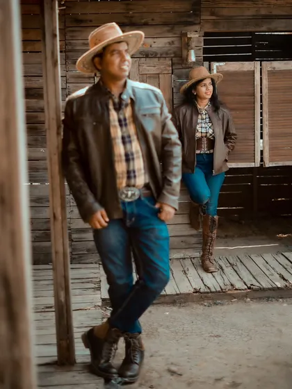 A cool, cowboy-themed pre-wedding shoot. Aditya and Priyanka look stylish in their leather jackets, hats, and boots against a rustic wooden backdrop.