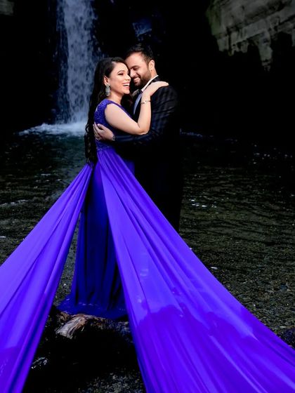 The dual trails of this royal blue gown create a stunning symmetrical effect, framing the couple perfectly against the dark waterfall background for a truly epic shot.