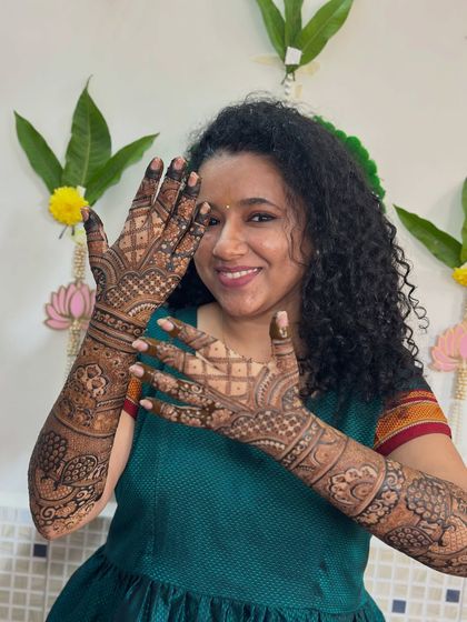 A happy bride showing off her beautiful, full-coverage mehendi. The design is packed with traditional motifs, creating a timeless bridal look.