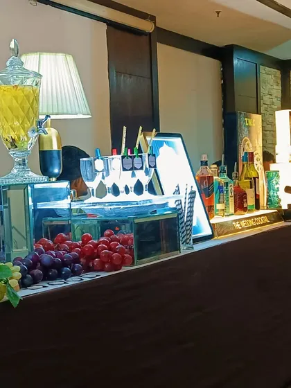 A close-up of a drink station featuring large glass dispensers for sangria or mocktails, fresh grapes for garnish, and a well-lit bar top.