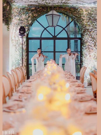 Violinists perform at the end of the long, elegant dinner table, adding to the sophisticated and romantic atmosphere.