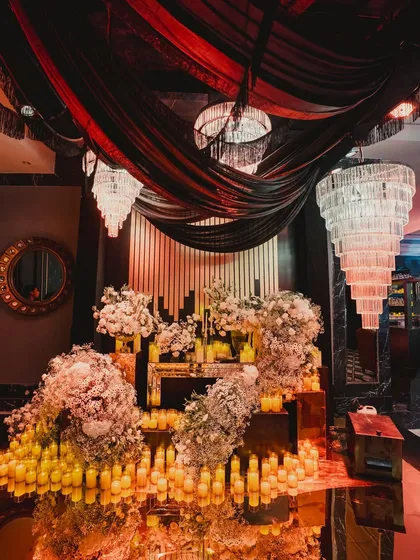 A stunning decor installation featuring cascading white florals, hundreds of candles, and dramatic black and red ceiling drapes.