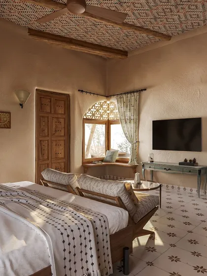 A corner window seat offers panoramic views of the surrounding nature. The patterned floor tiles and woven textiles on the bed add a layer of artisanal charm to this tranquil guest room.