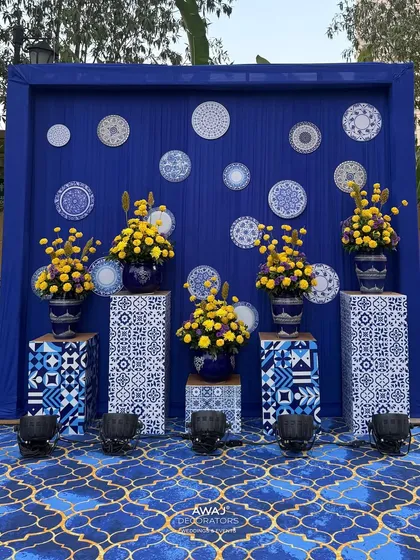 A photo-op backdrop with a wall of decorative plates and vibrant floral arrangements in matching blue and white vases.