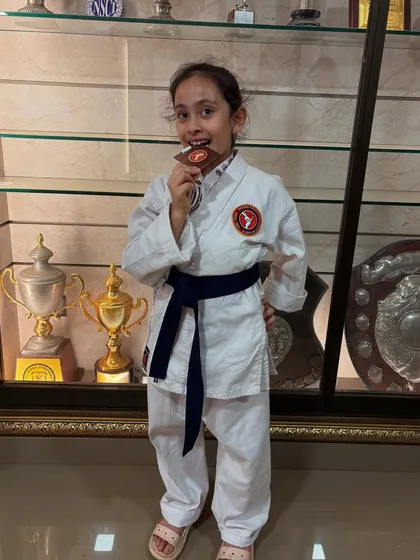 A champion's smile. This young student proudly bites her bronze medal, a classic pose celebrating her hard-earned victory at the academy's tournament.