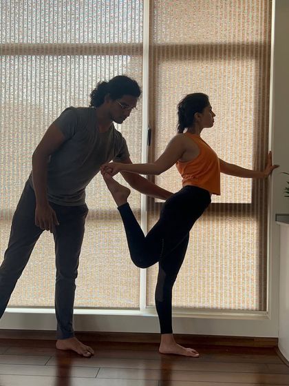 An instructor guides a student into Natarajasana (Dancer's Pose), helping her find the balance between effort and ease in this graceful posture.