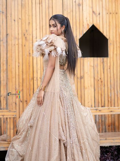 An elegant beige gown with unique feather details on the shoulders. This full-length shot showcases the drama and craftsmanship of the designer outfit.