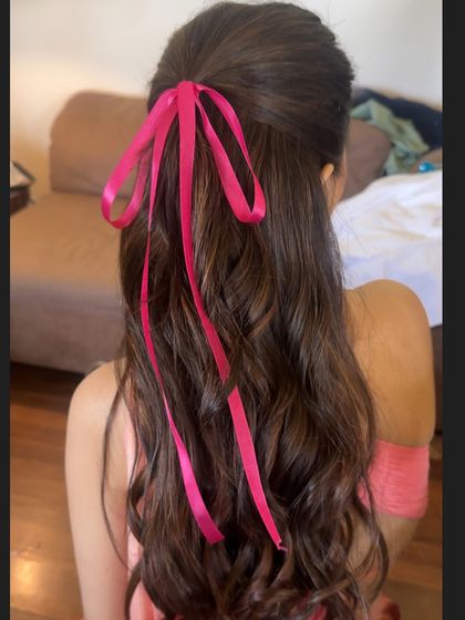 A romantic half-updo with soft waves, tied with a simple yet striking hot pink ribbon. This coquette-inspired hairstyle is perfect for a bridal shower or a fun pre-wedding photoshoot.
