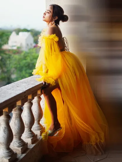 An artistic shot of actress Manisha Rani on a balcony, using a slow shutter speed to capture the flowing movement of her gown. This style adds a dreamy, editorial quality to promotional photos.