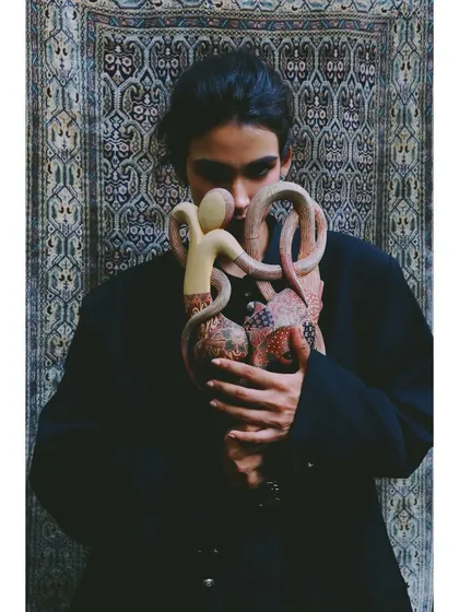 The model holds the mask close, as if protecting a precious part of her identity. The styling here is simple, focusing on the emotional connection to the cultural artifact.