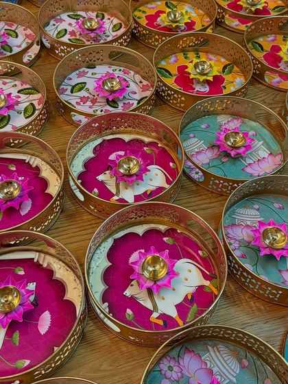 A collection of decorative trays used as part of a bulk order for wedding return favors. Each tray features unique, colorful Indian folk art designs.