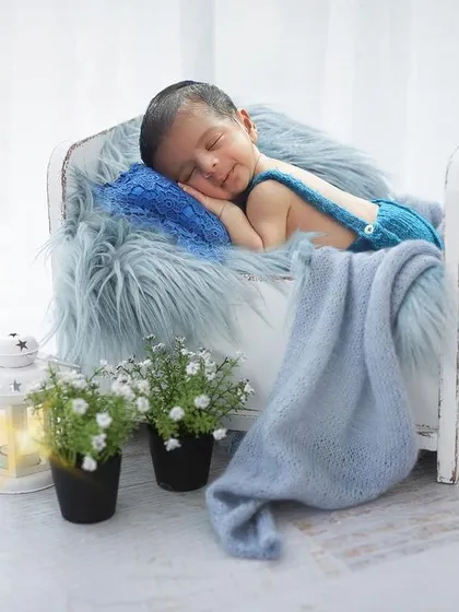 A peaceful portrait with a cool blue color palette. This baby boy is sleeping on a miniature bed with a soft blue blanket and fur, creating a serene and dreamy atmosphere.