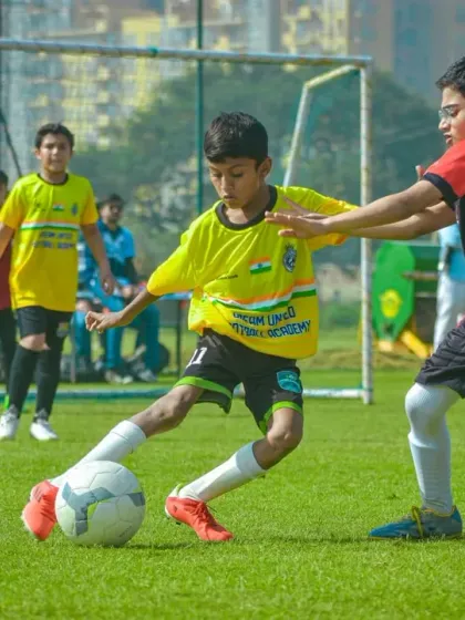 A player in a yellow jersey shields the ball from a defender, demonstrating strength and smart positioning.