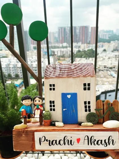 Simplicity at its best. This nameplate features a charming, rustic miniature house with a blue door, a couple figurine, and a tiny bicycle. It’s a perfect reflection of a simple, unhurried life, handcrafted to bring a sense of peace to your home.