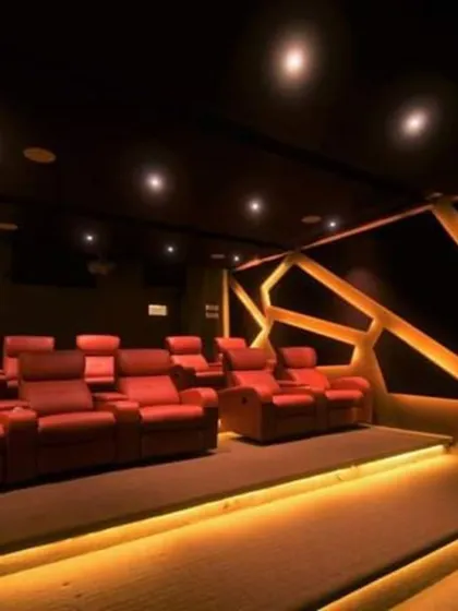 We customize the color palette and layout to your taste. This vibrant theater features bold red recliners on a raised platform for optimal viewing, complemented by warm, geometric wall lighting to enhance the ambiance.