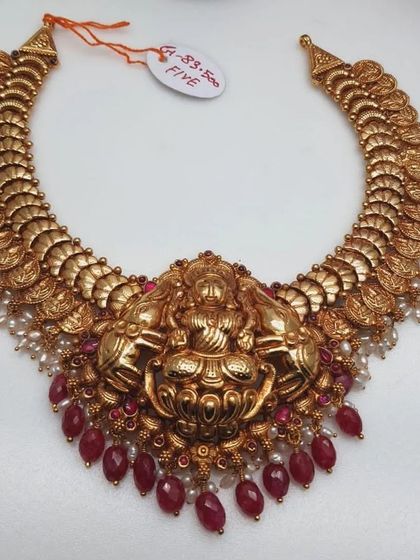 This grand kasu mala (coin necklace) features a large Goddess Lakshmi pendant. Made from 92.5 silver with gold plating, it is embellished with ruby beads and pearls.