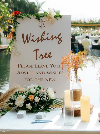A beautifully designed sign for the wishing tree, surrounded by pampas grass and floral arrangements that match the event's aesthetic.